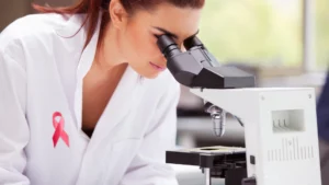 Mujer con bata blanca y un lazo rosa en la solapa, observando por un microscopio.